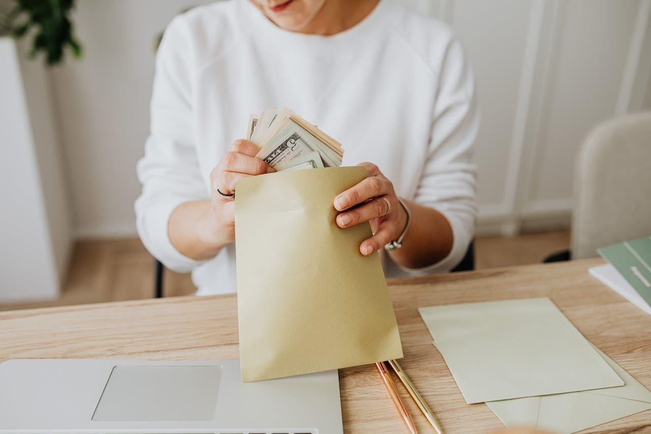Hands placing U.S. dollar bills into an envelope, representing predictable rental income and cash flow from U.S. real estate investments