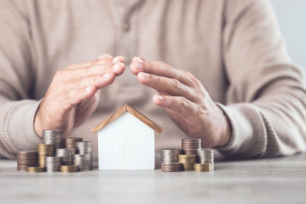 Hands protecting a small house model surrounded by coins, representing institutional-grade capital protection and disciplined risk controls in real estate investing